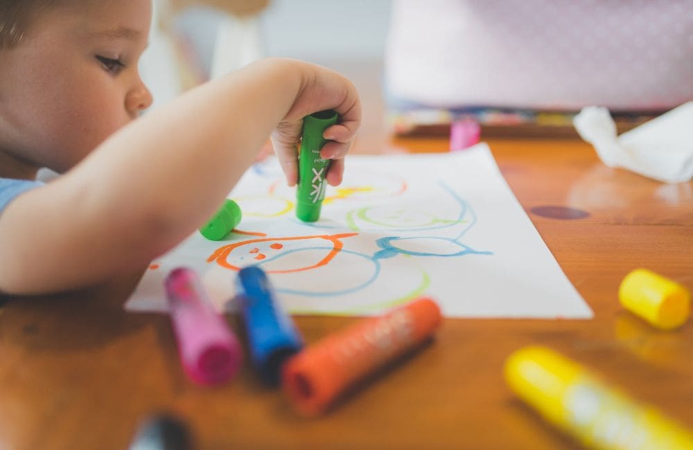 young child drawing on a piece of paper with markers in childcare